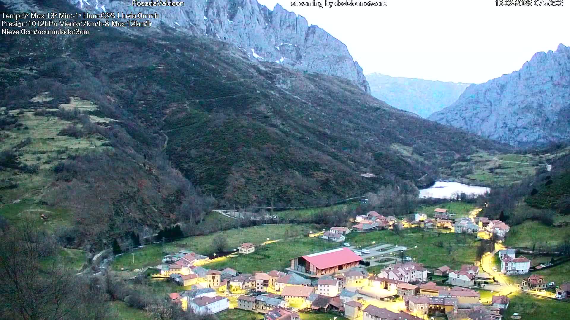 A small village nestled in a valley between mountains at twilight, illuminated by streetlights.