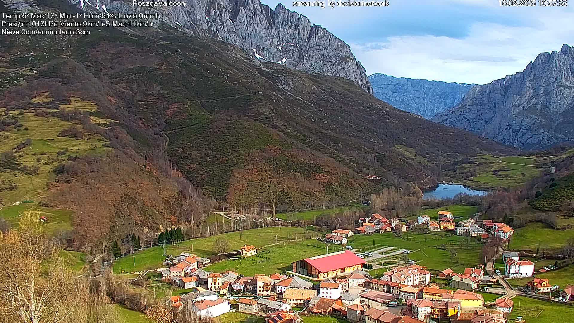 A small village nestled in a valley between steep, rocky mountains under a partly cloudy sky.