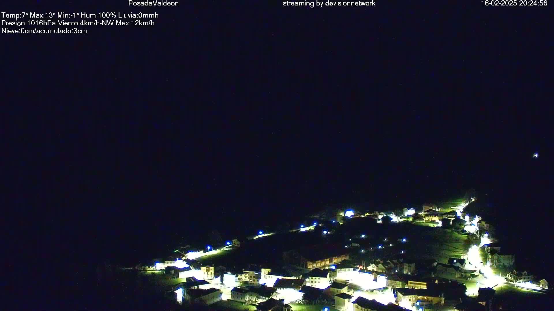 A nighttime, aerial view of a small village illuminated by streetlights under a dark, clear sky.