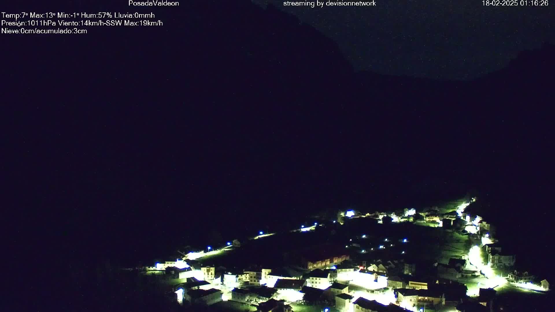 A small village illuminated at night sits nestled in a valley under a dark, clear sky.