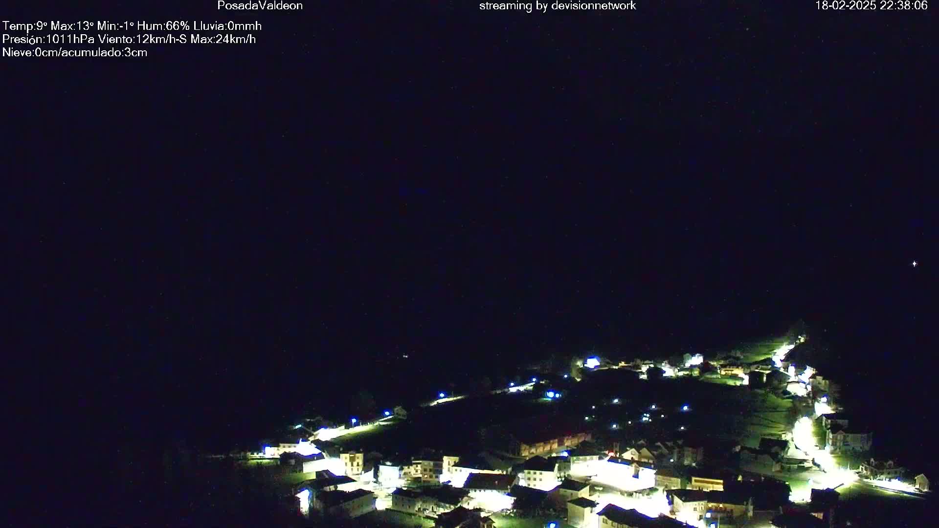 A nighttime aerial view of a small village illuminated by lights under a dark, clear sky.