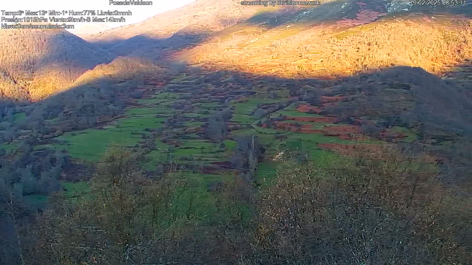 A sunlit hillside with terraced fields and sparse, leafless trees is visible in a mountainous landscape.