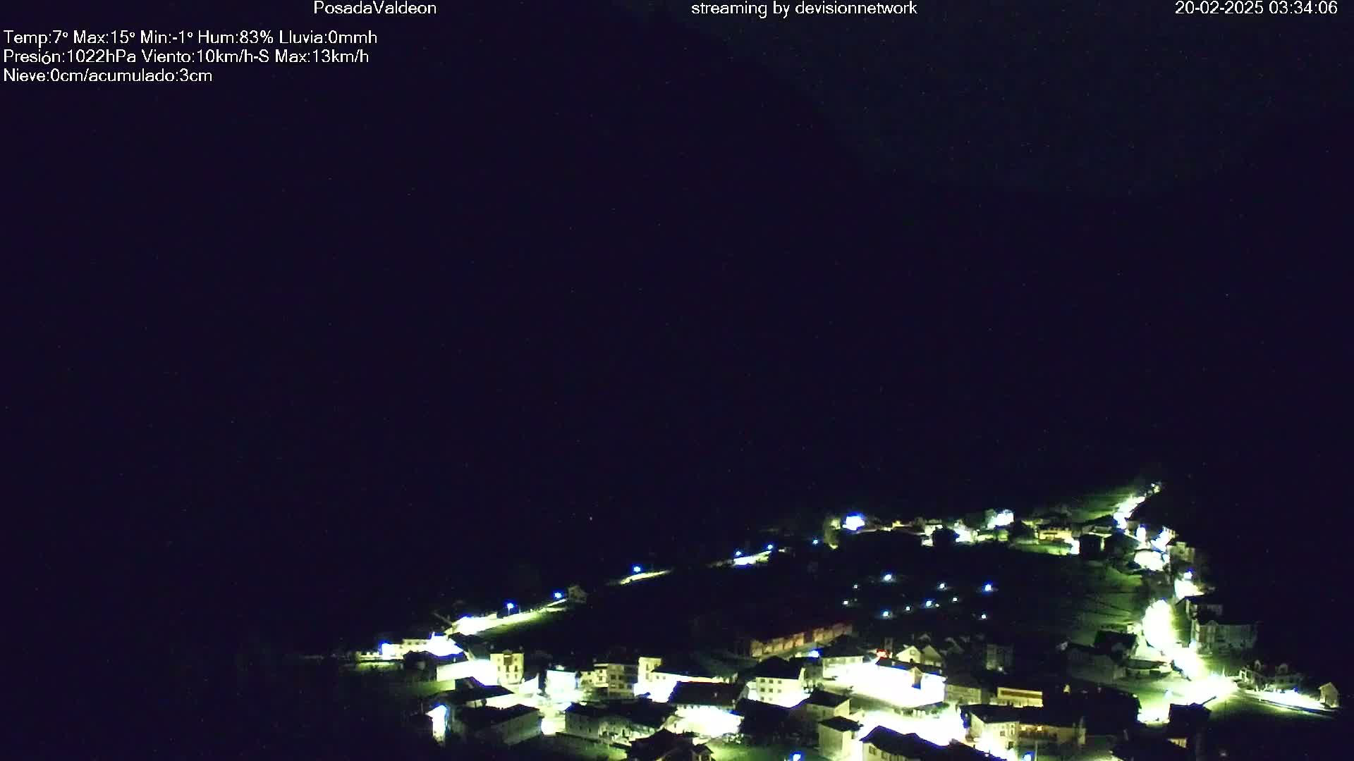 A small village at night, illuminated by its streetlights, is nestled in a dark, mountainous area under a clear, black sky.
