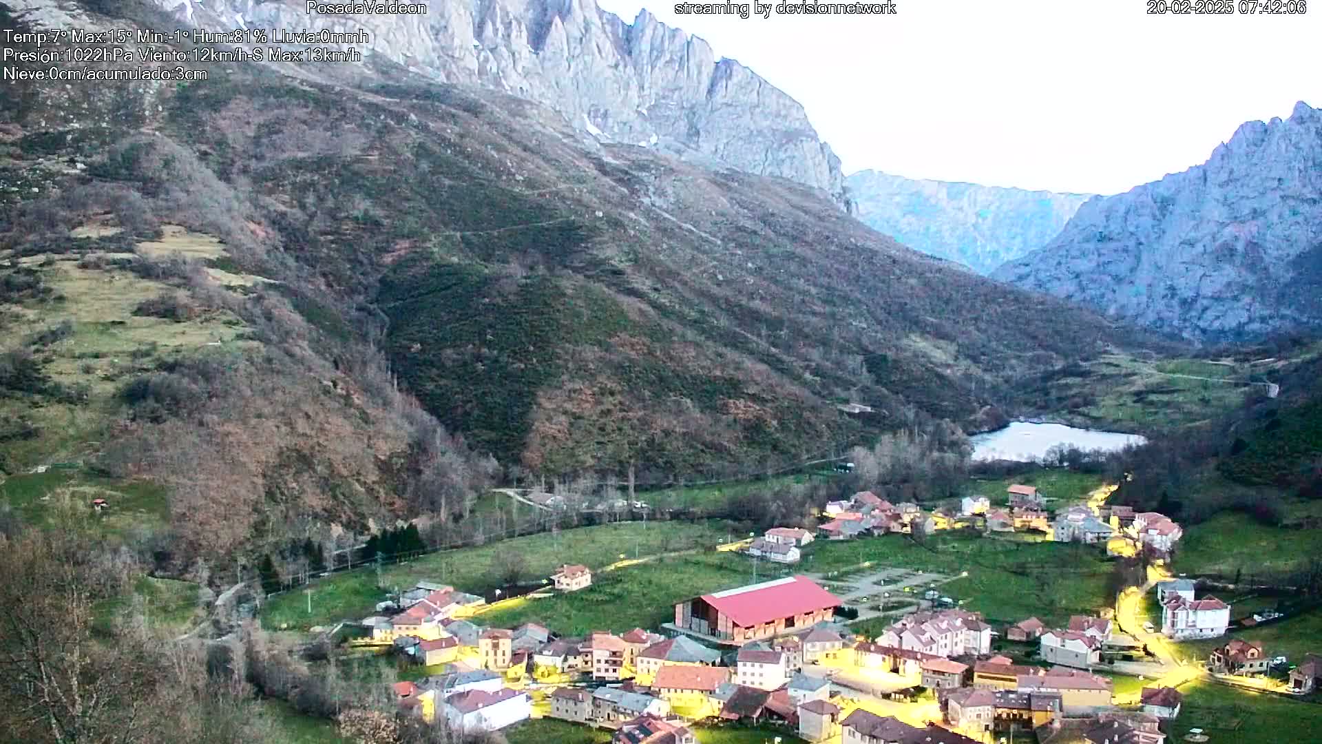 A small village nestled in a valley between tall mountains at dusk, with lights illuminating the buildings.