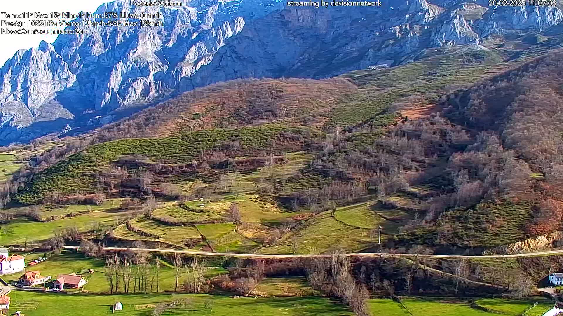 A sunny, rural valley scene with a road winding through it, nestled beneath a mountainous backdrop.