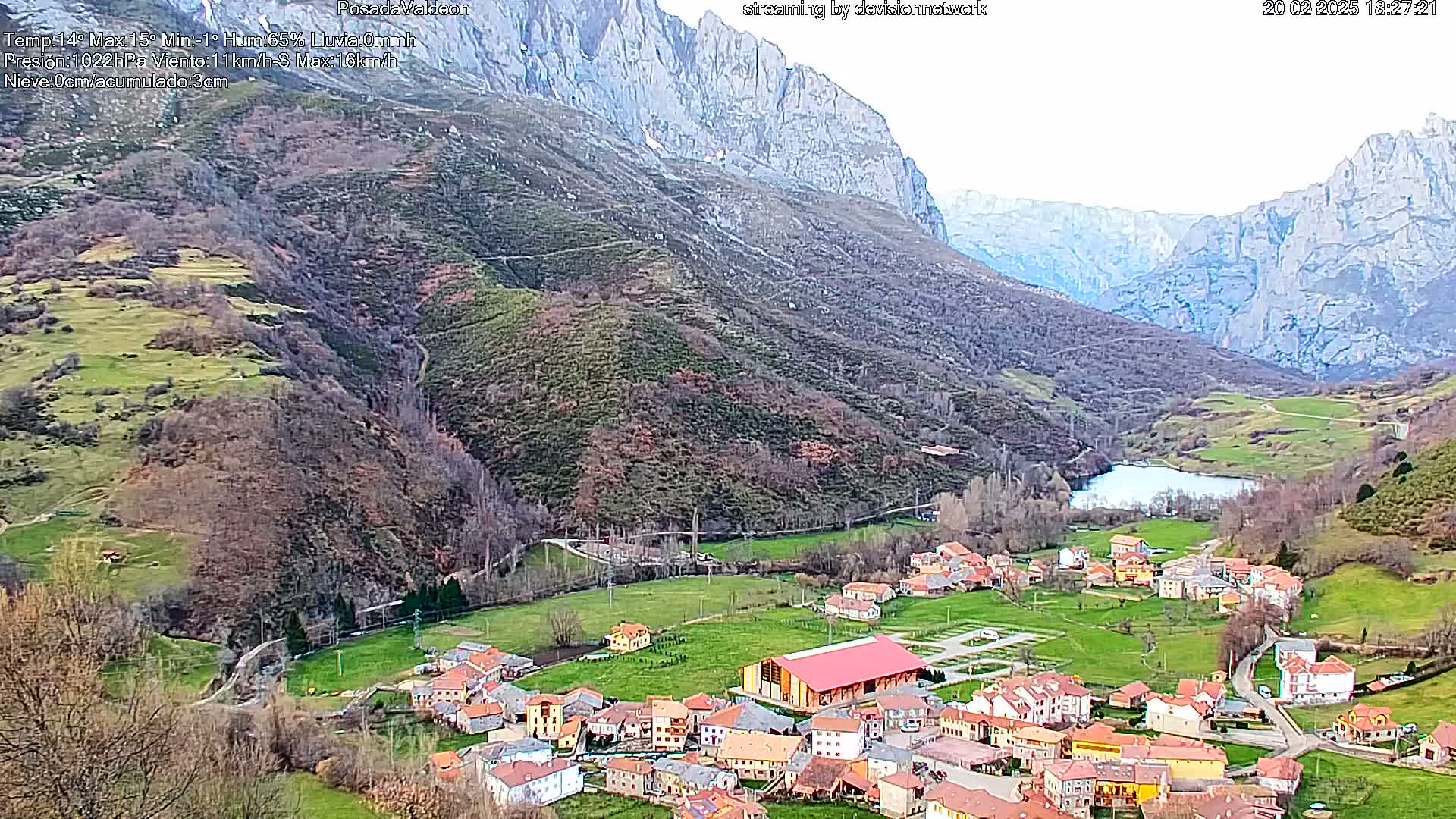 A small village nestled in a valley between large, rocky mountains under a mostly clear sky.
