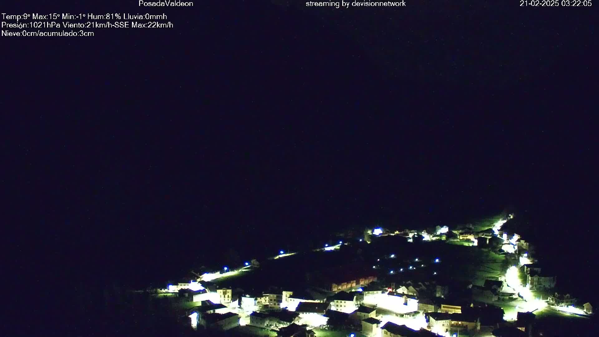 A nighttime aerial view shows a small village illuminated by lights under a dark, clear sky.