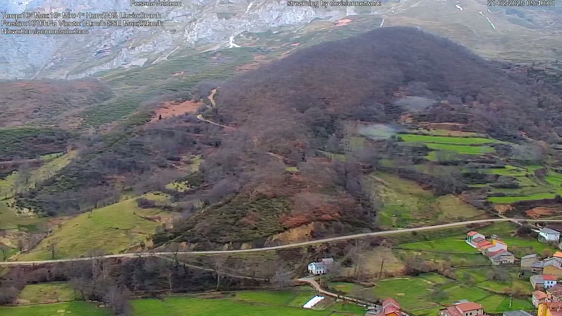 An aerial view shows a mountainous landscape with a small village nestled in a valley, under overcast skies.