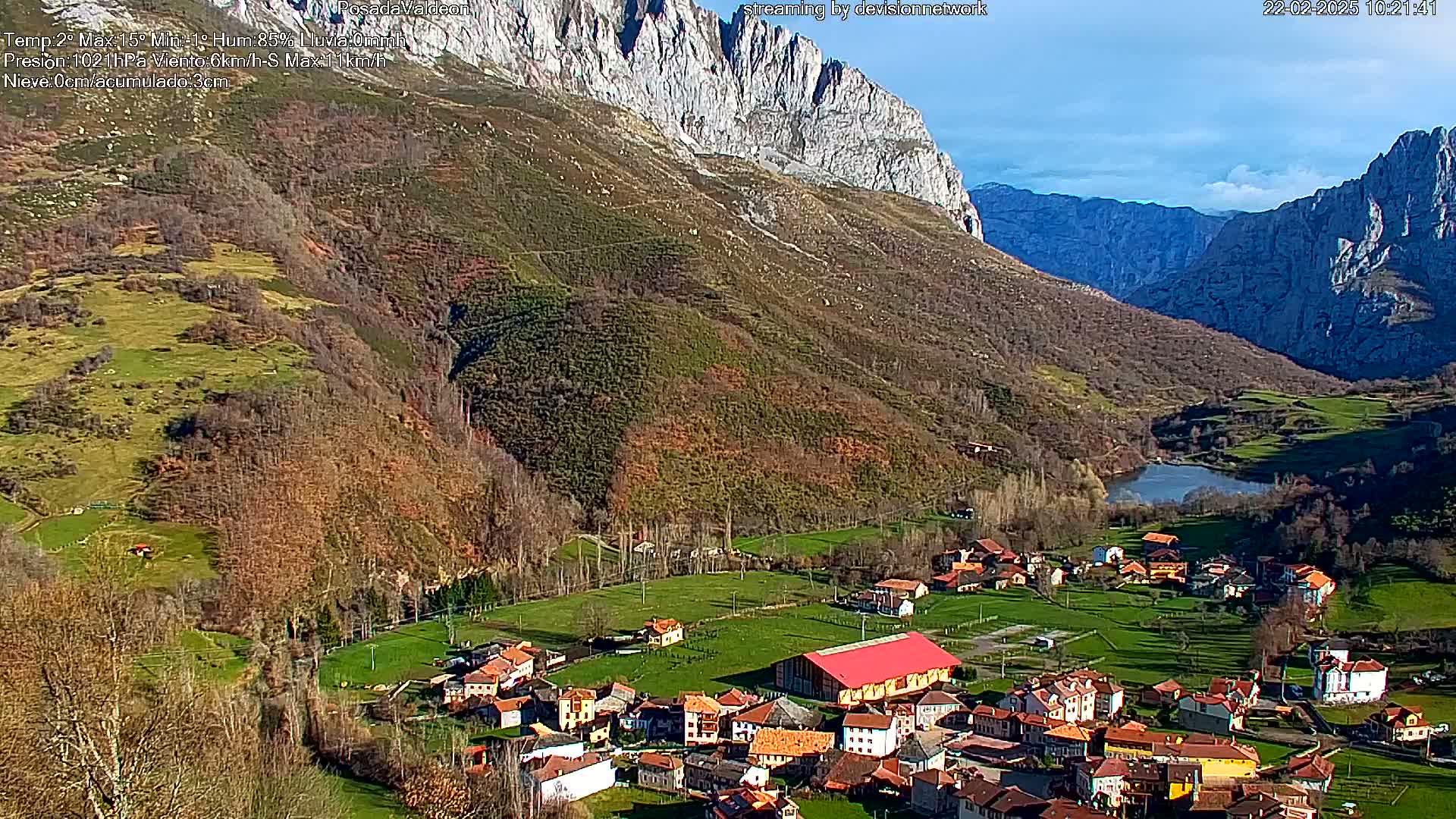 A small village nestled in a valley between steep, rocky mountains under a mostly sunny sky.