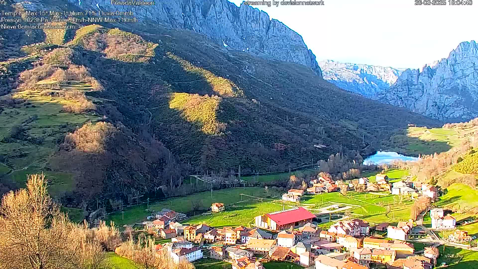 A small village nestled in a valley between towering, rocky mountains, bathed in the sunlight of a clear day.