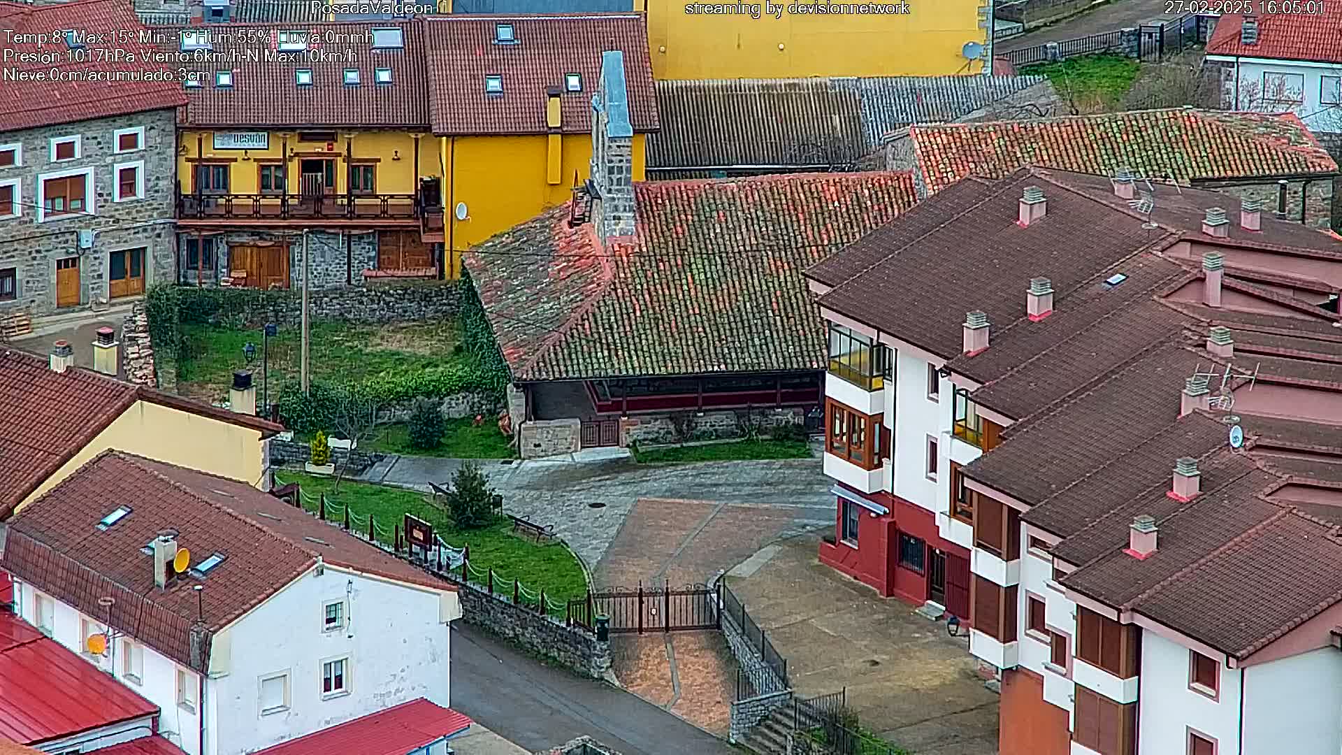 An aerial view of a village with red-tiled roofs, including a building that may be a church, on an overcast day.