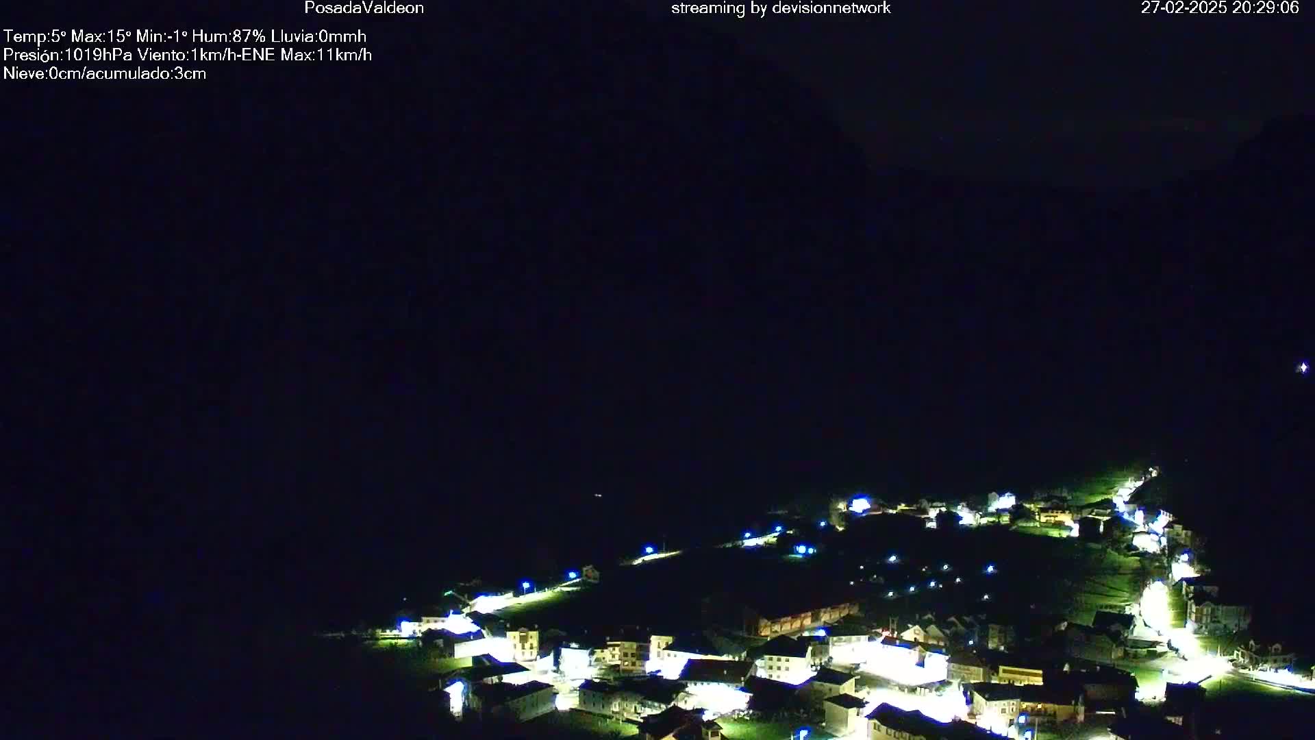 A nighttime, long shot of a small village illuminated by lights under a dark, clear sky.