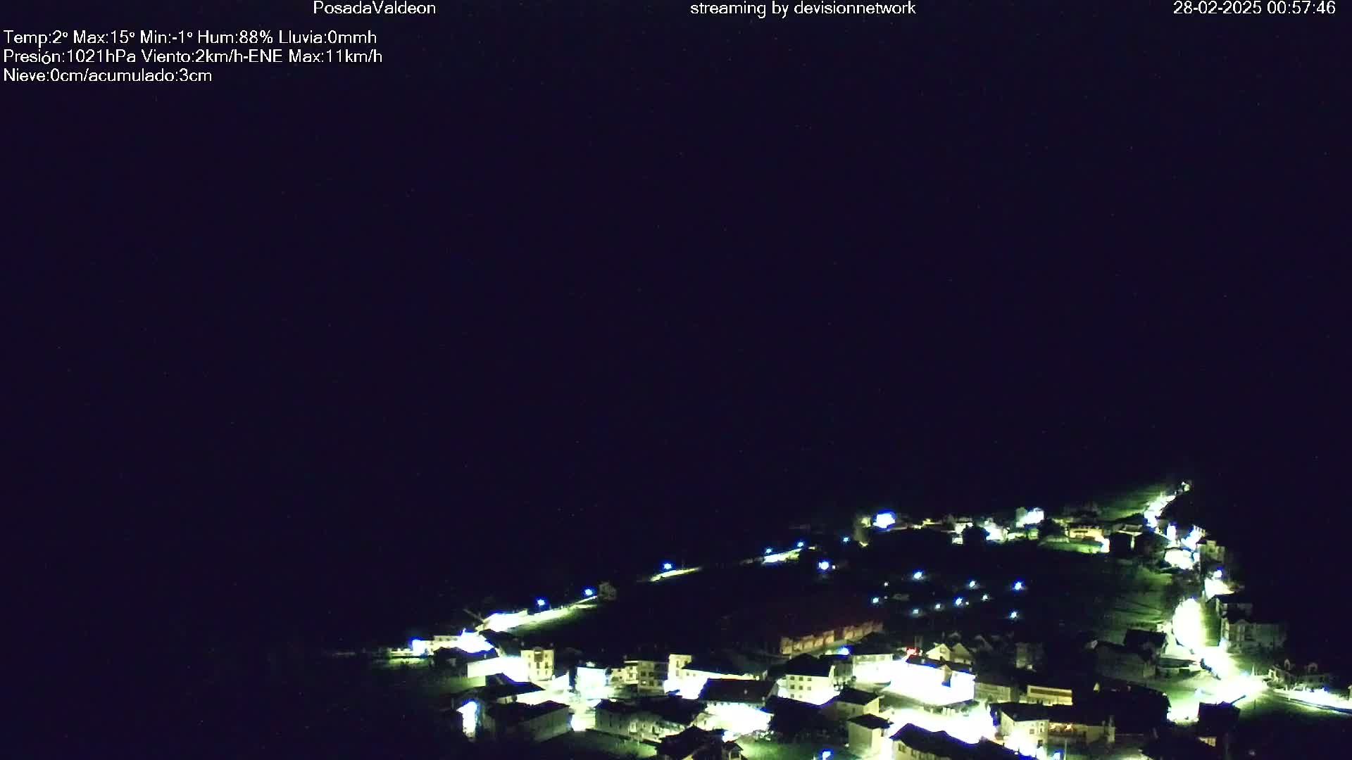 A nighttime aerial view of a small village illuminated by streetlights under a clear, dark sky.