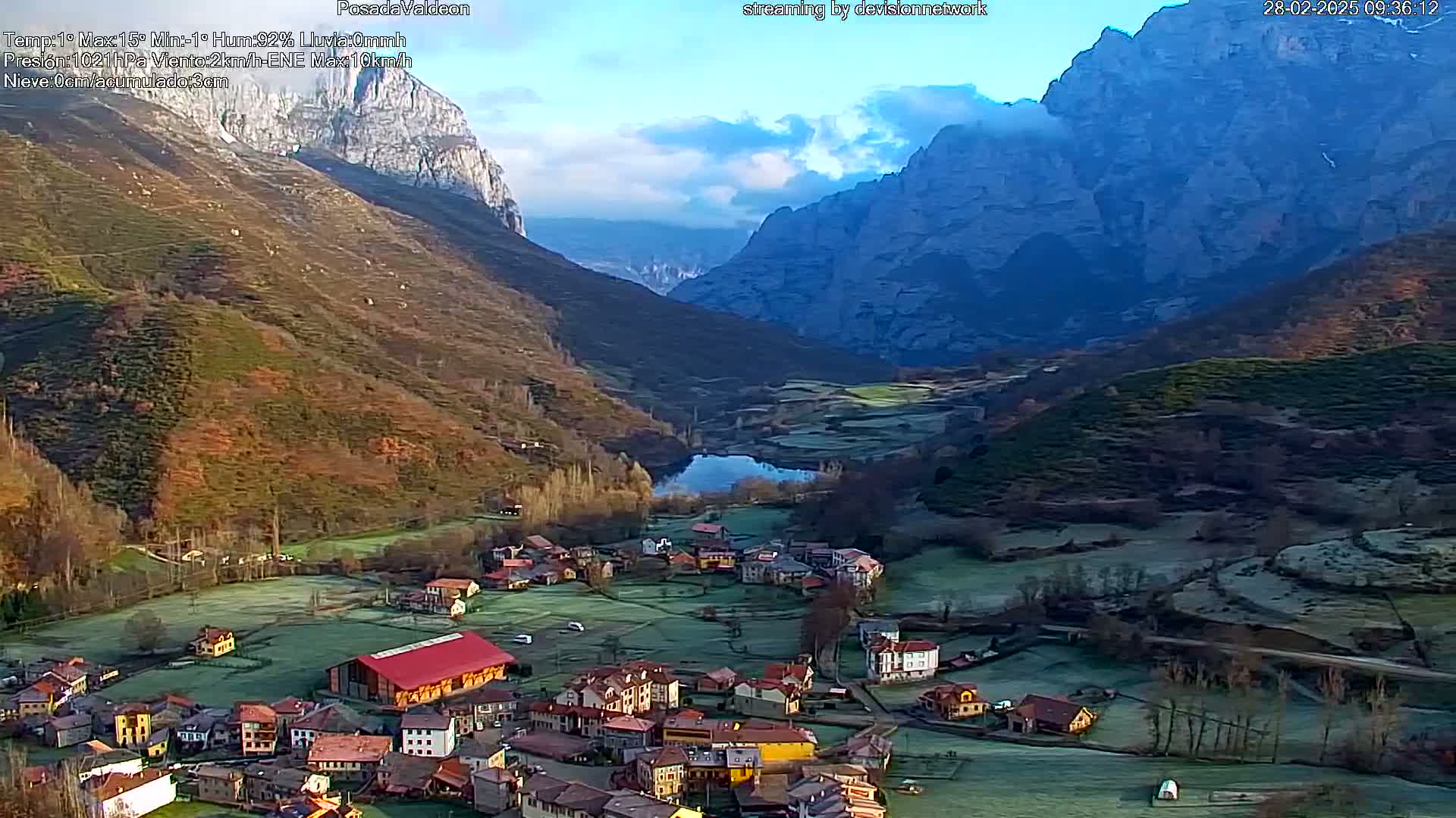 A frost-covered village nestled in a valley between towering mountains under a partly cloudy sky.