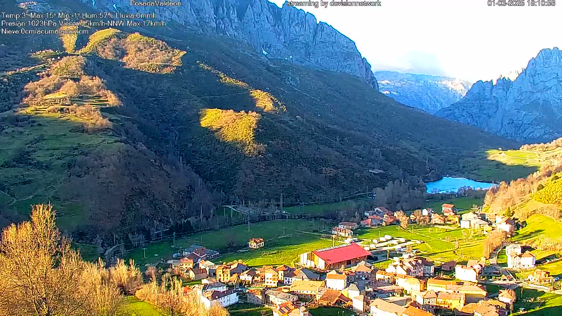 A small village nestled in a valley between tall, rocky mountains, under a mostly clear sky.