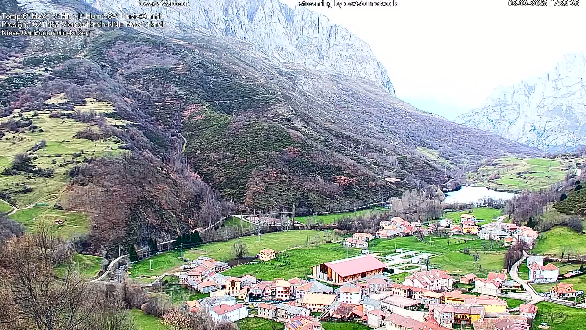 A small village nestled in a verdant valley between towering, rocky mountains under an overcast sky.