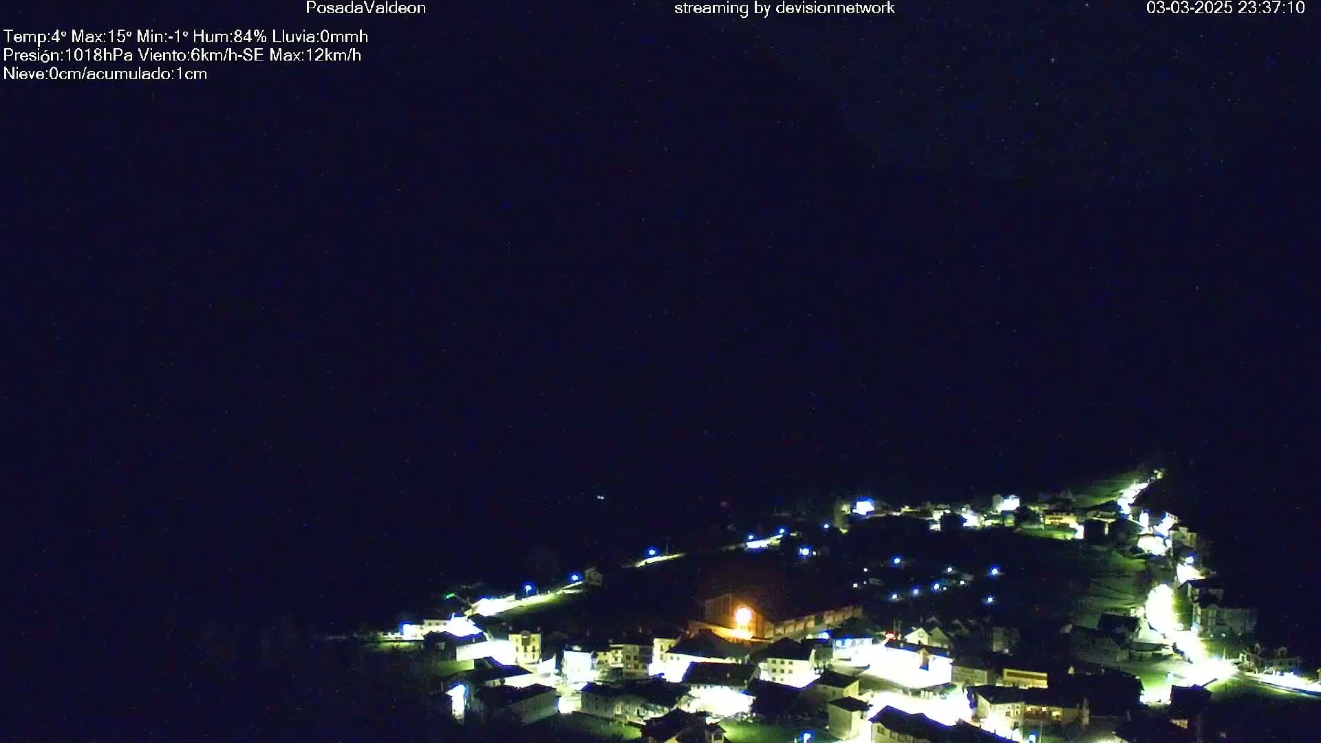 A small, illuminated village is nestled in a dark, nighttime landscape under a clear sky.