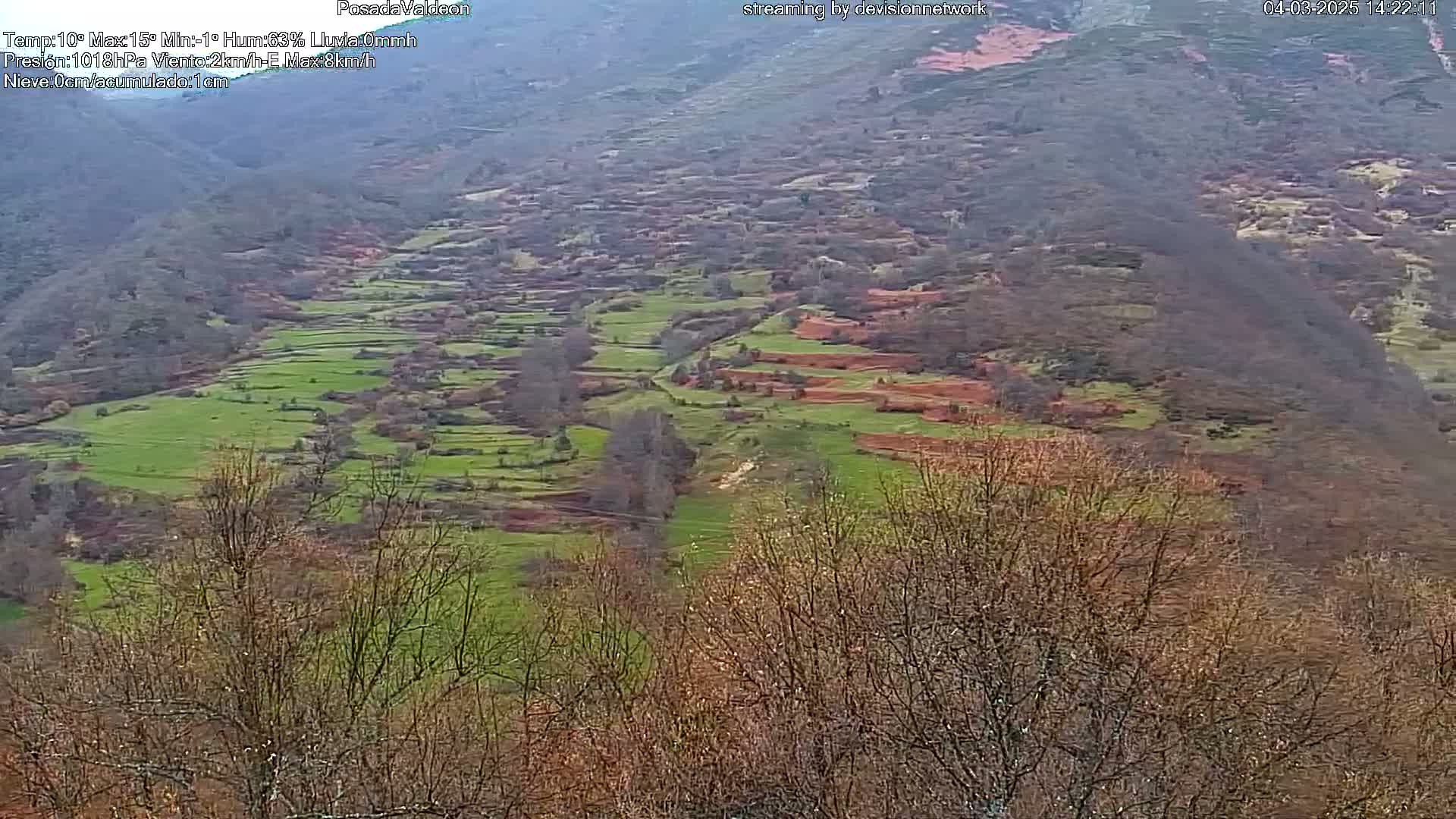 A hilly landscape with patches of green grass and reddish-brown earth is visible from a distance, under an overcast sky.