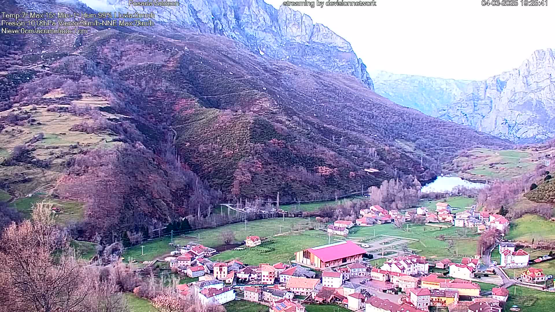 A small village nestled in a valley between steep, rocky mountains, under a mostly clear sky.
