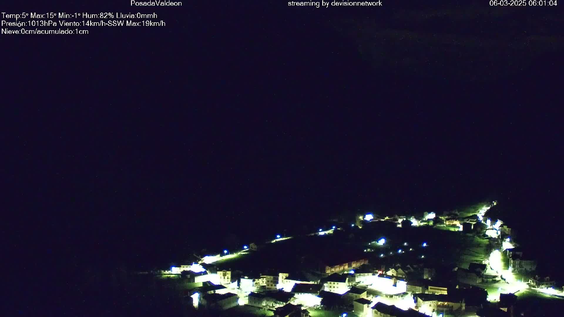 A small, illuminated village is nestled in a dark, nighttime landscape under a clear, dark sky.
