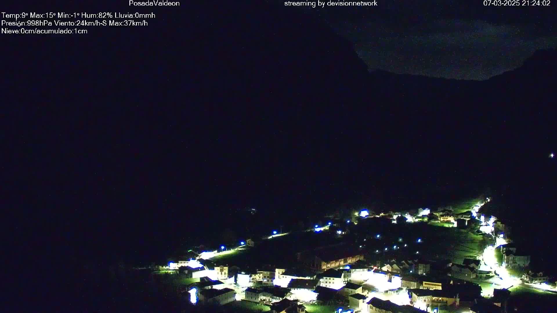 A small, illuminated village nestled in a dark valley under a mostly clear night sky.
