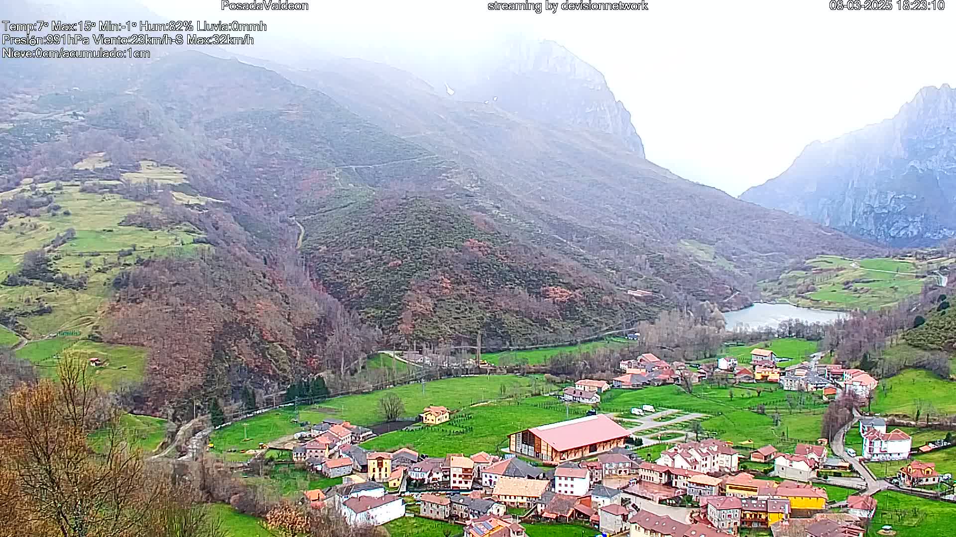 A small village nestled in a valley between misty mountains, with a lake visible in the valley below.