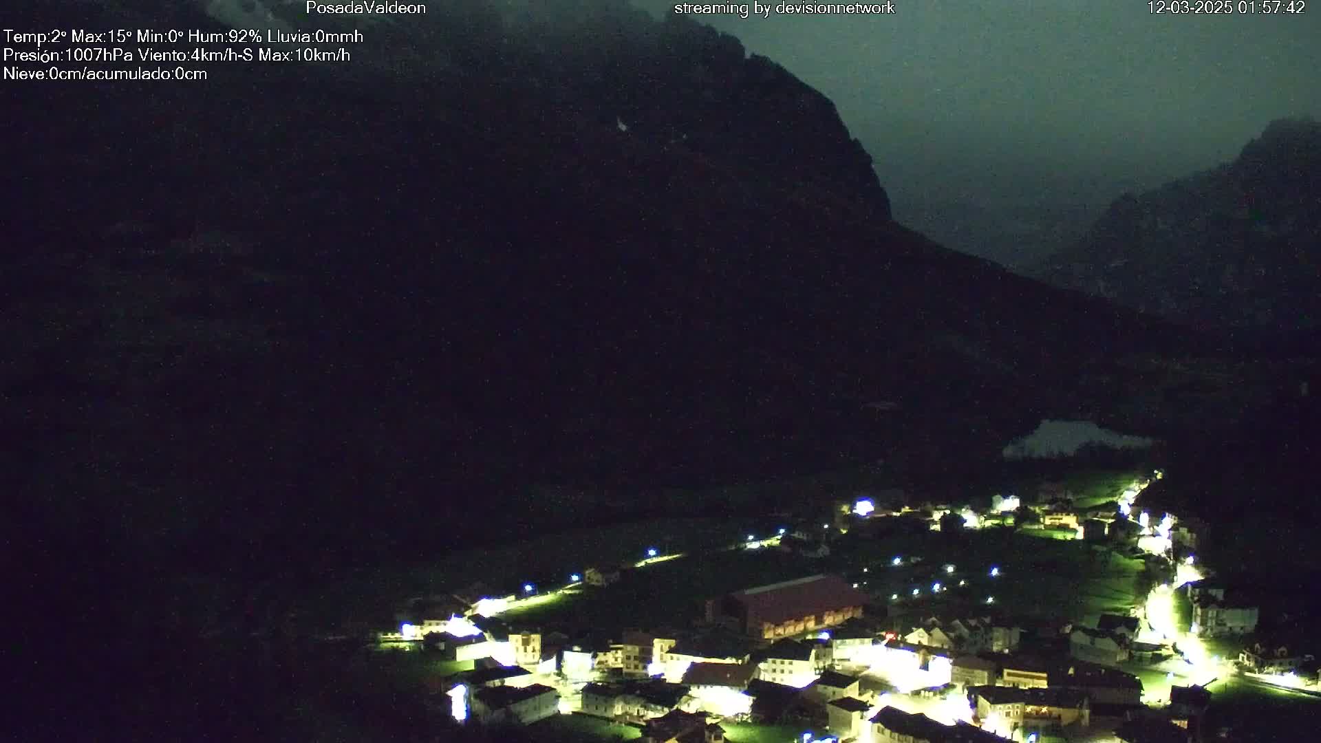A small, illuminated village nestled at the base of a dark mountain under a nighttime sky.