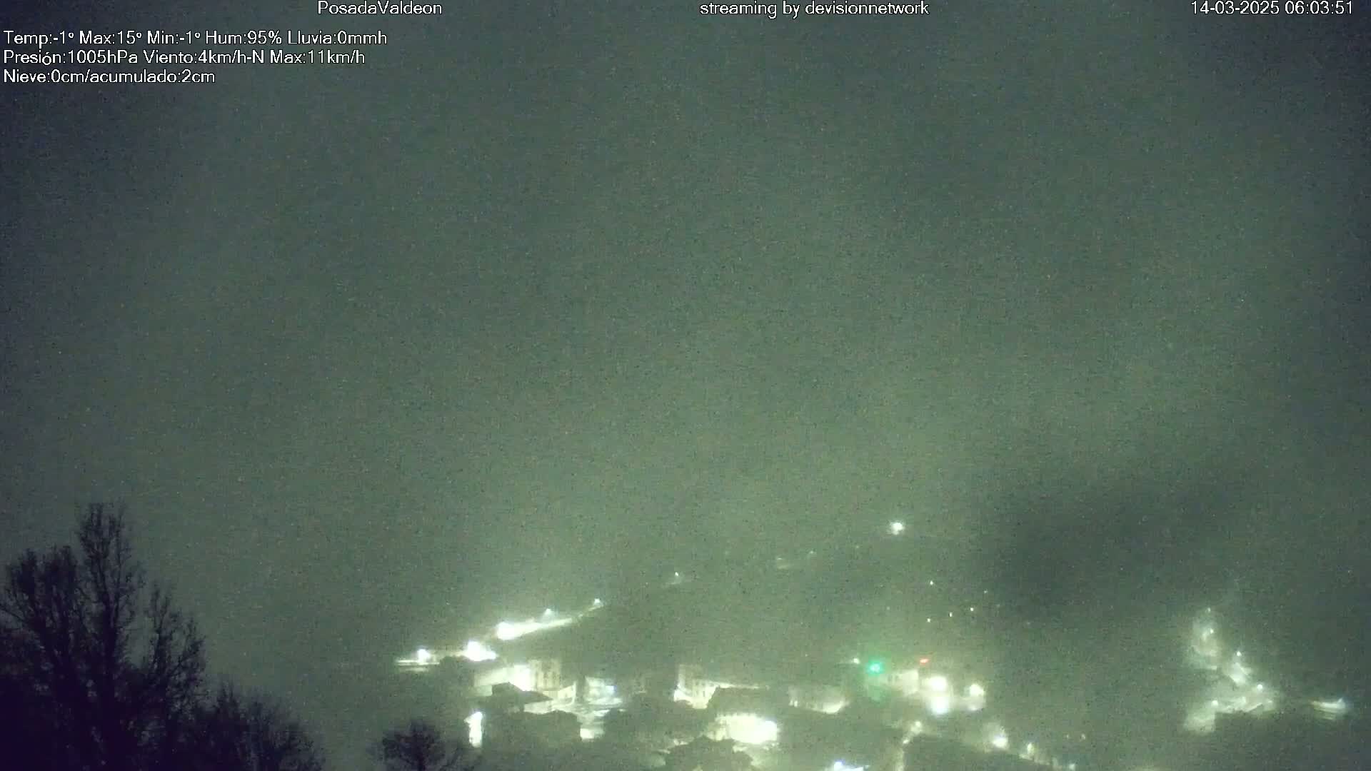 A nighttime view of a town shrouded in fog, with dimly lit buildings visible below.