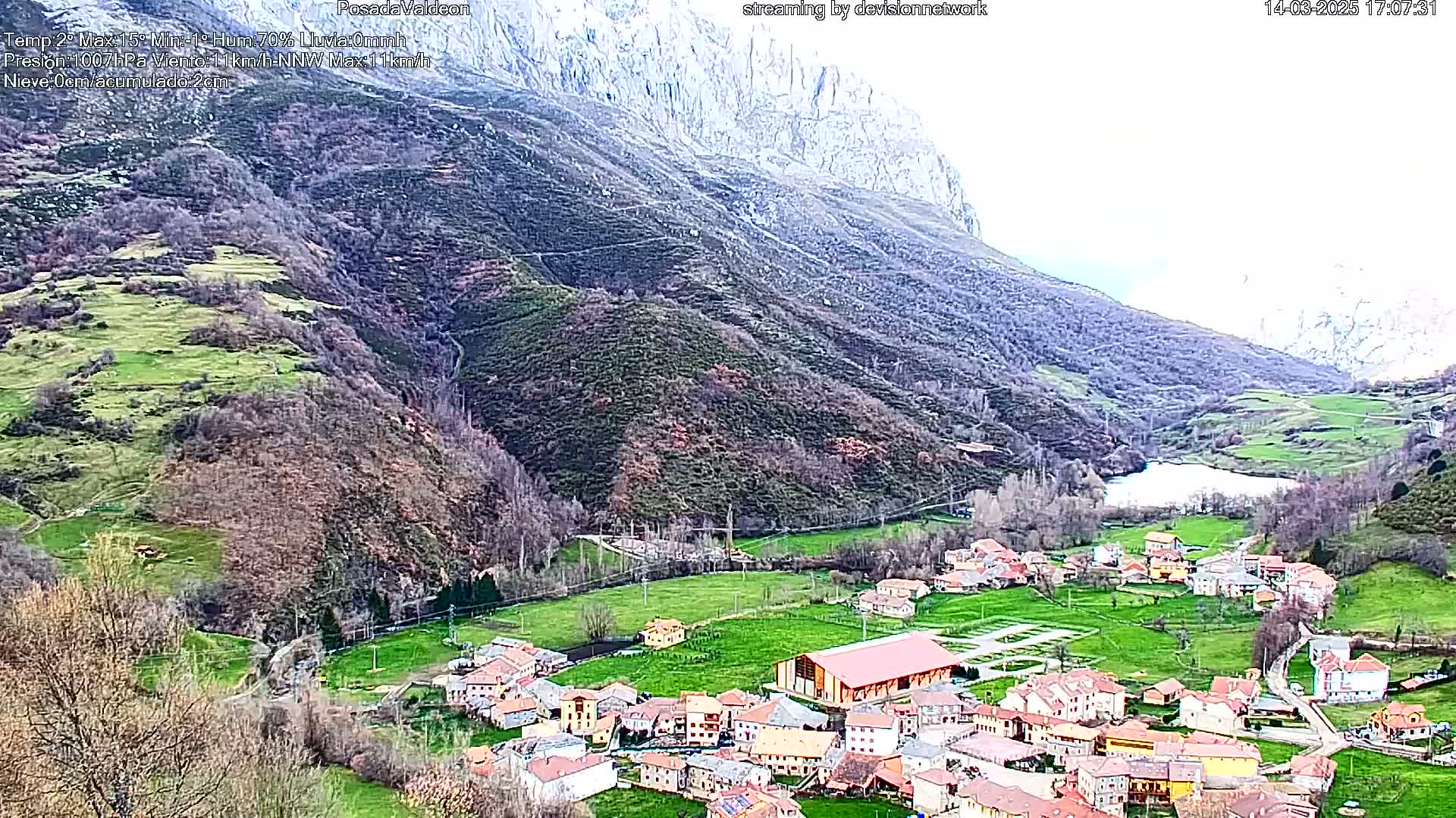 A small village nestled in a verdant valley, surrounded by mountains under an overcast sky.