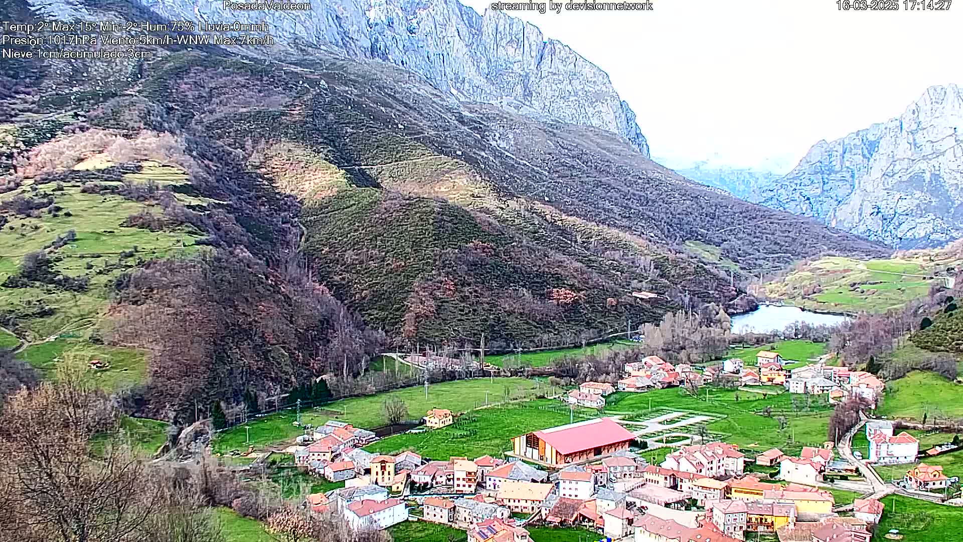 A small village nestled in a valley between steep, rocky mountains, under a mostly clear sky.