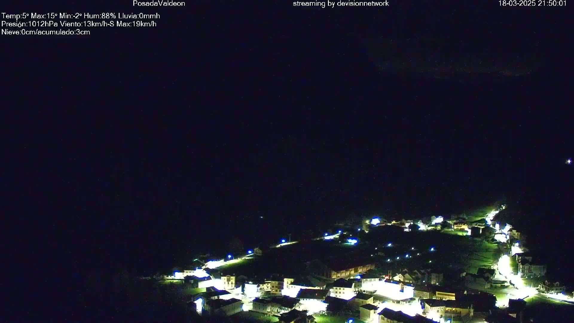 A small, illuminated village is nestled in a dark, nighttime landscape under a clear sky.
