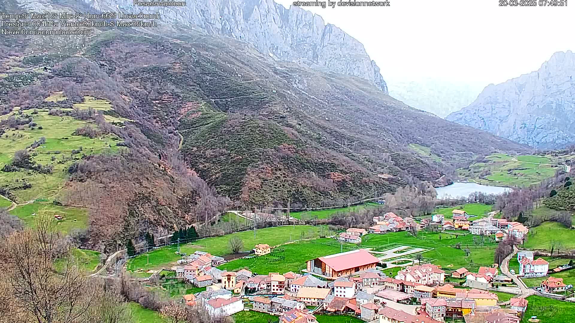 A small village nestled in a valley between mountains, under an overcast sky.