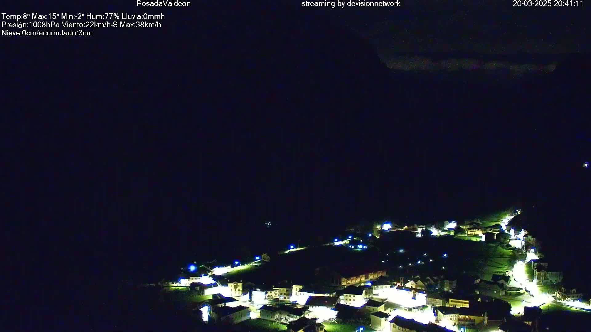 A nighttime aerial view of a small, illuminated village nestled in a dark valley under a mostly clear sky.