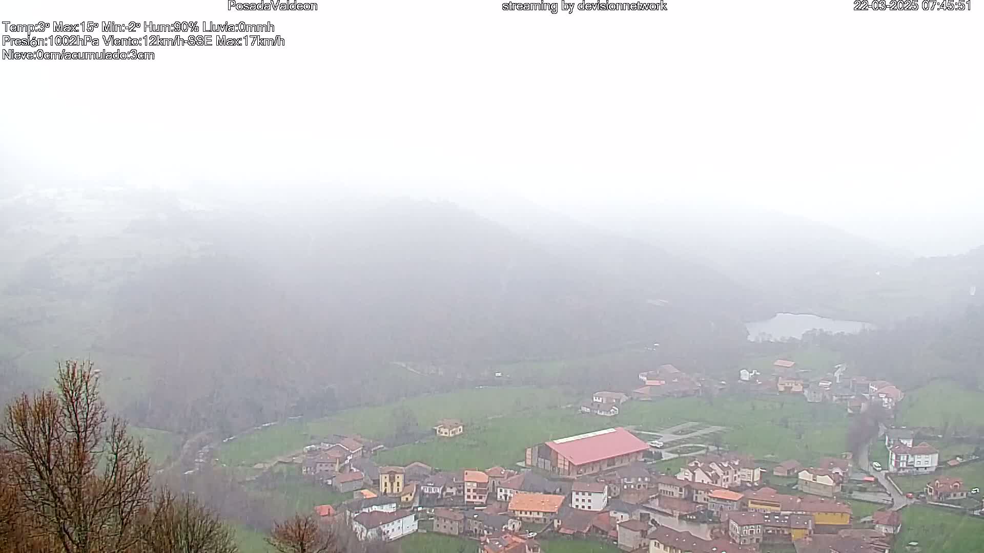 A foggy, elevated view of a small village nestled in a valley, with a body of water visible in the distance.