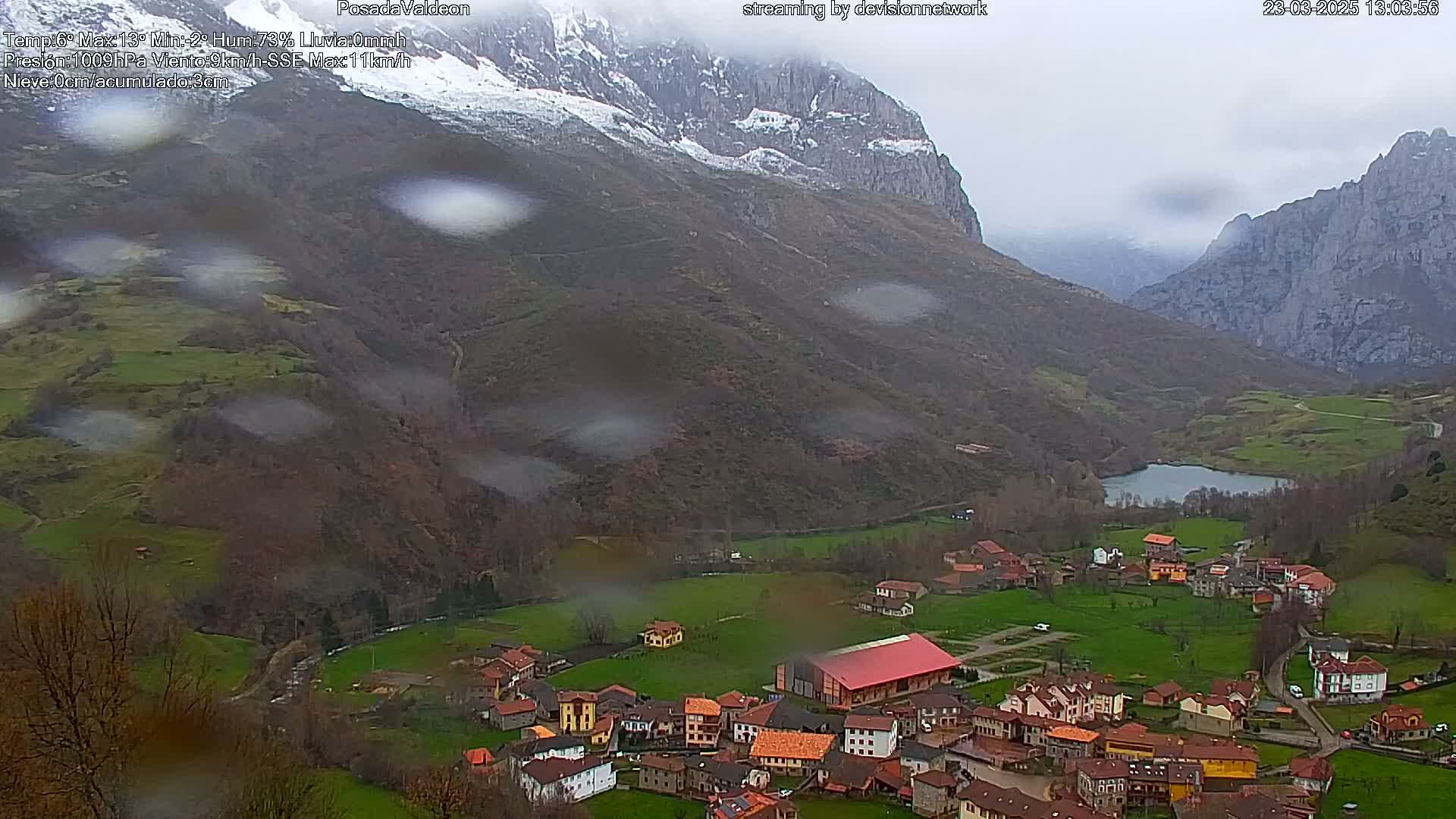 Rain falls on a small village nestled in a valley between snow-capped mountains.