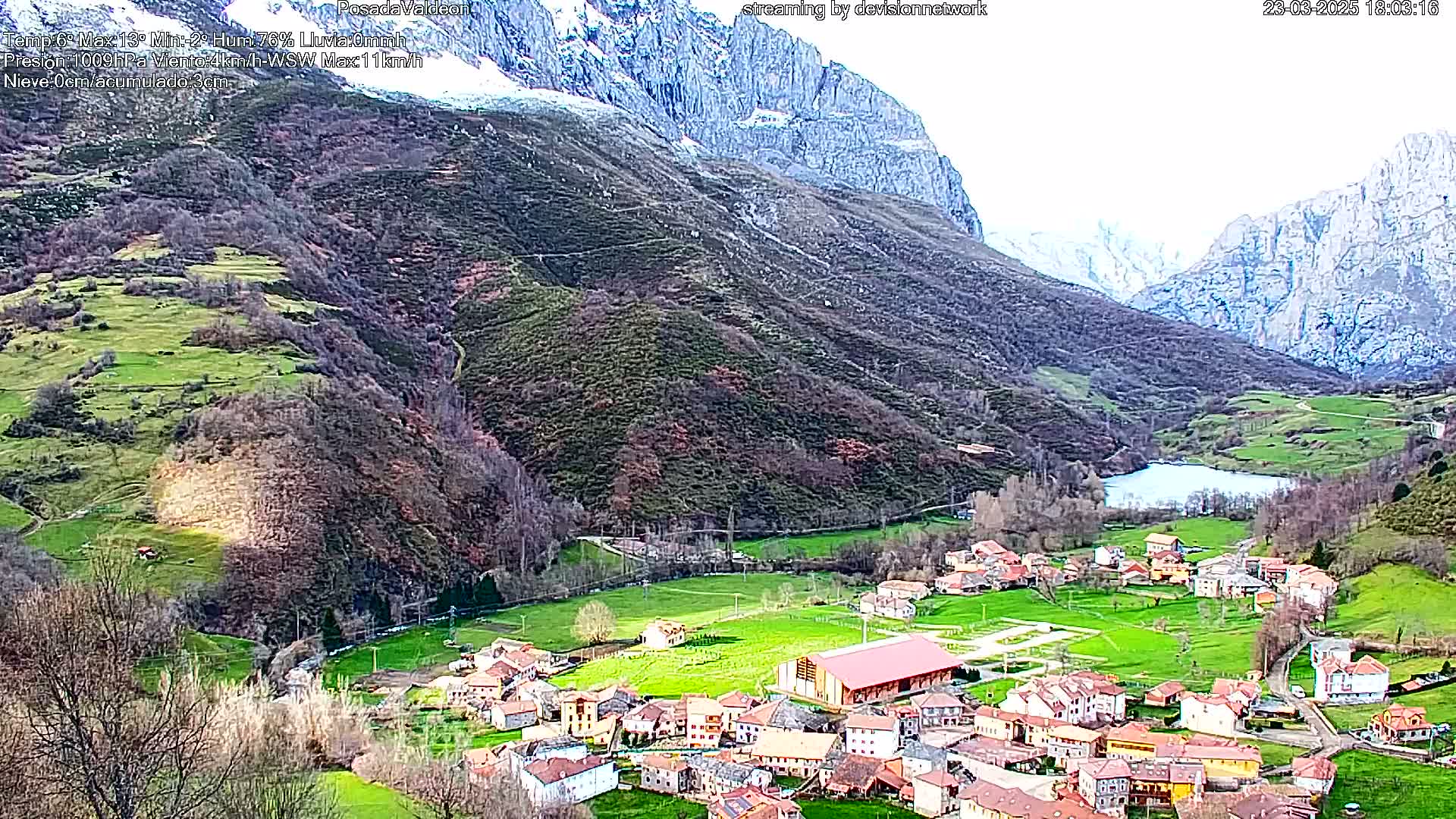 A small village nestled in a valley between snow-capped mountains under a partly cloudy sky.