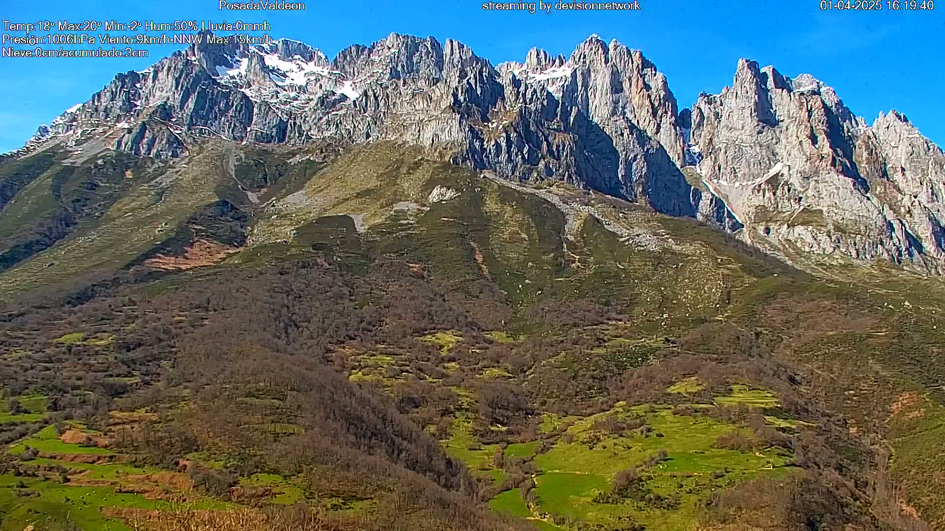A snow-capped mountain range rises above a valley of mostly brown and green vegetation under a clear blue sky.