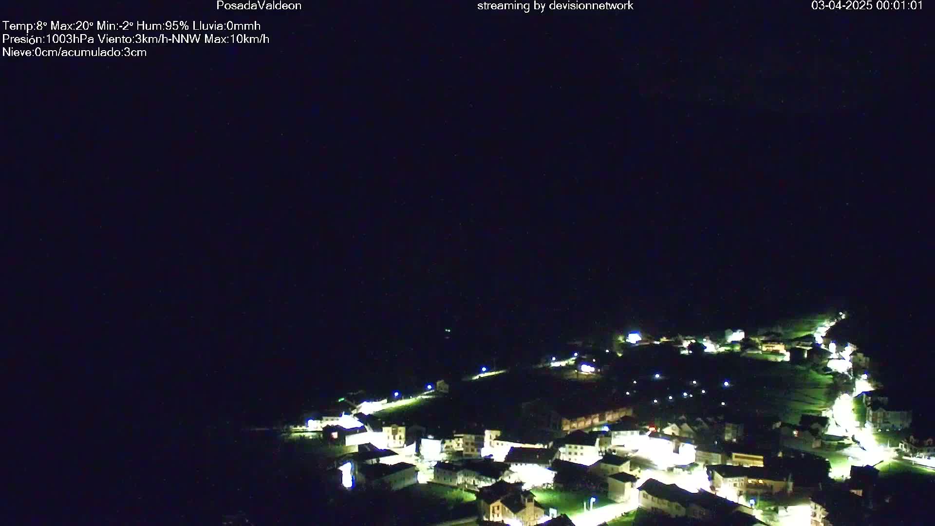 A small village at night is illuminated by lights, under a dark, clear sky.