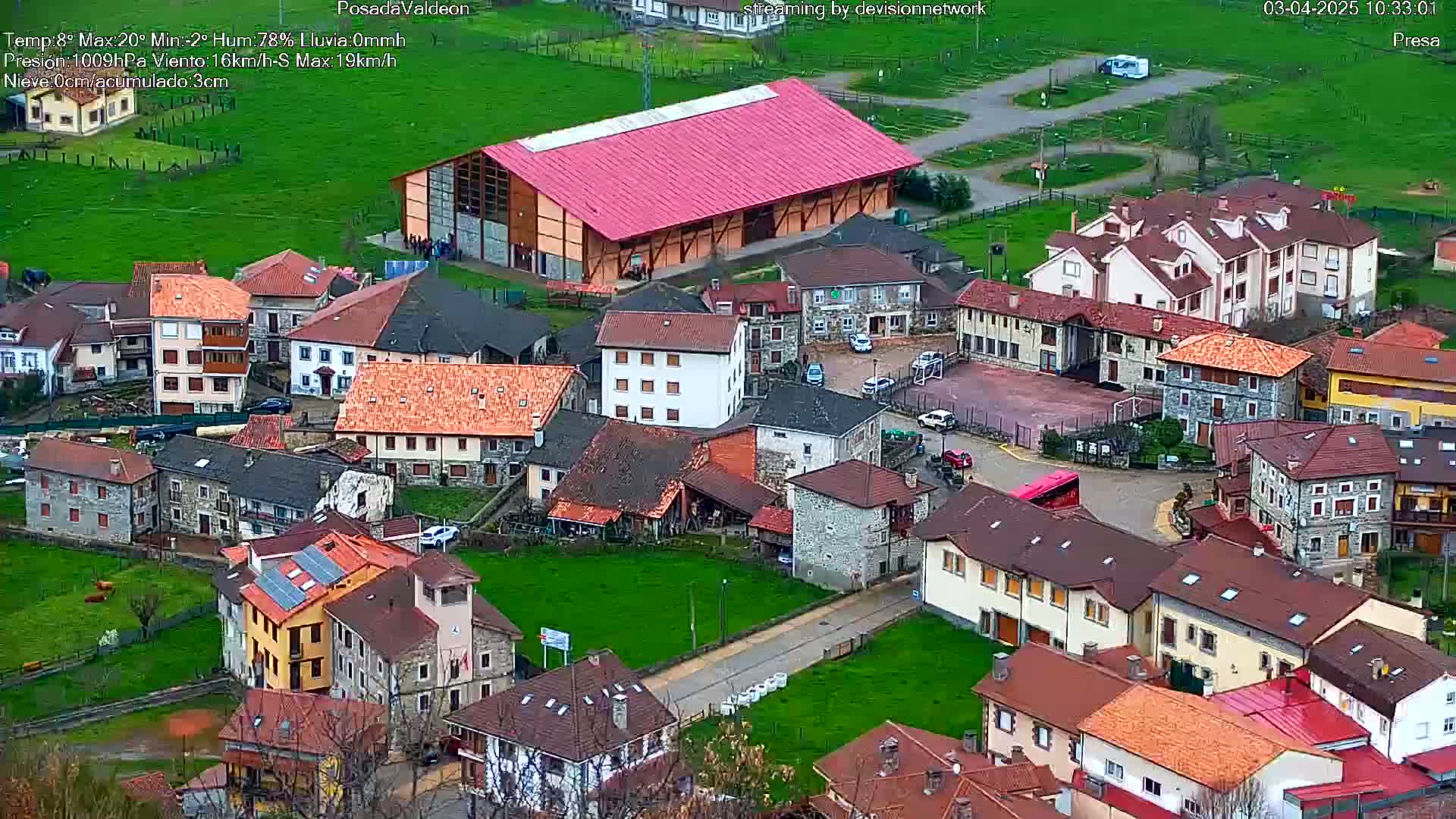 An aerial view shows a small village with stone and tile-roofed houses under a cloudy sky.