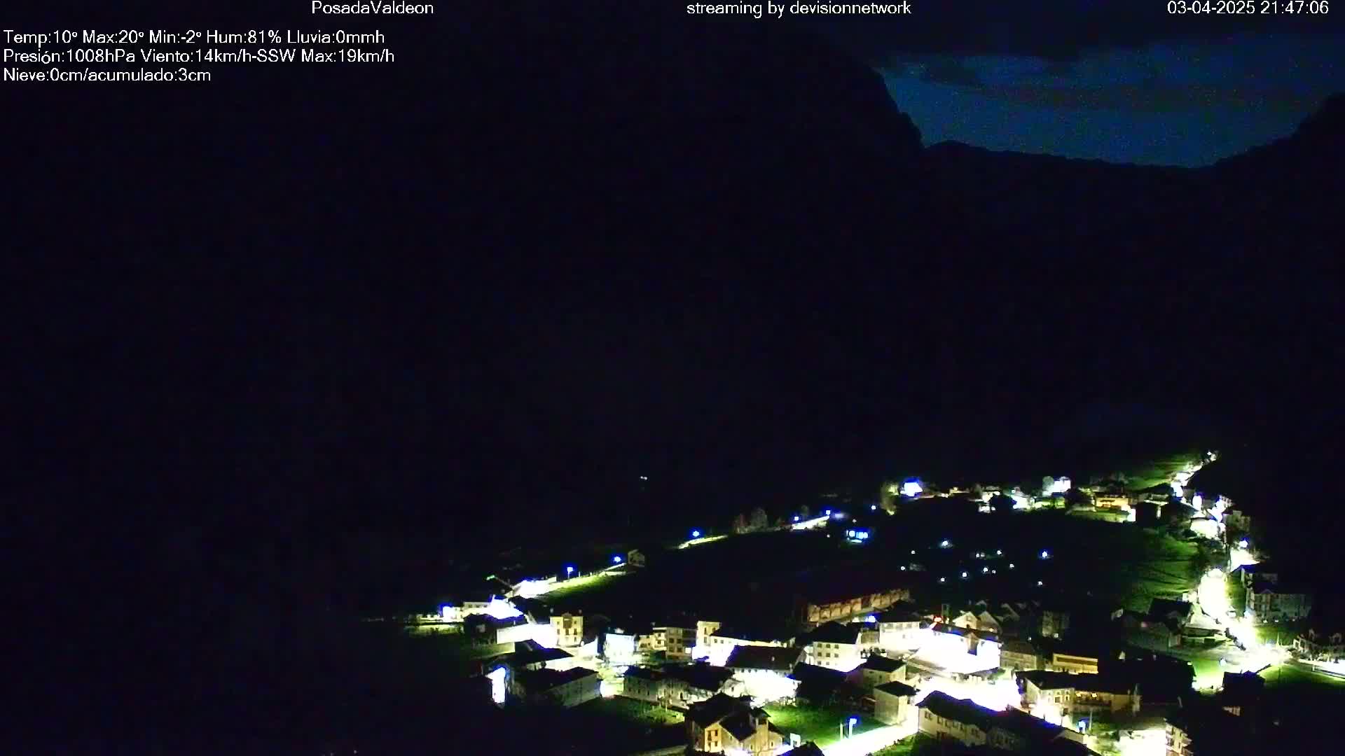 A nighttime, aerial view of a small village nestled in a dark valley under a mostly clear, dark sky.