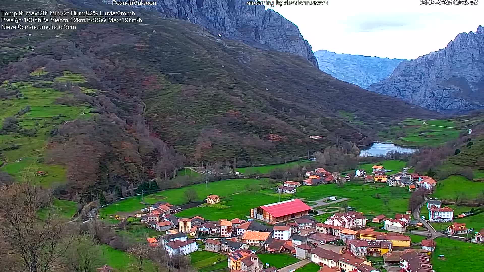 A small village nestled in a verdant valley between steep, rocky mountains under an overcast sky.