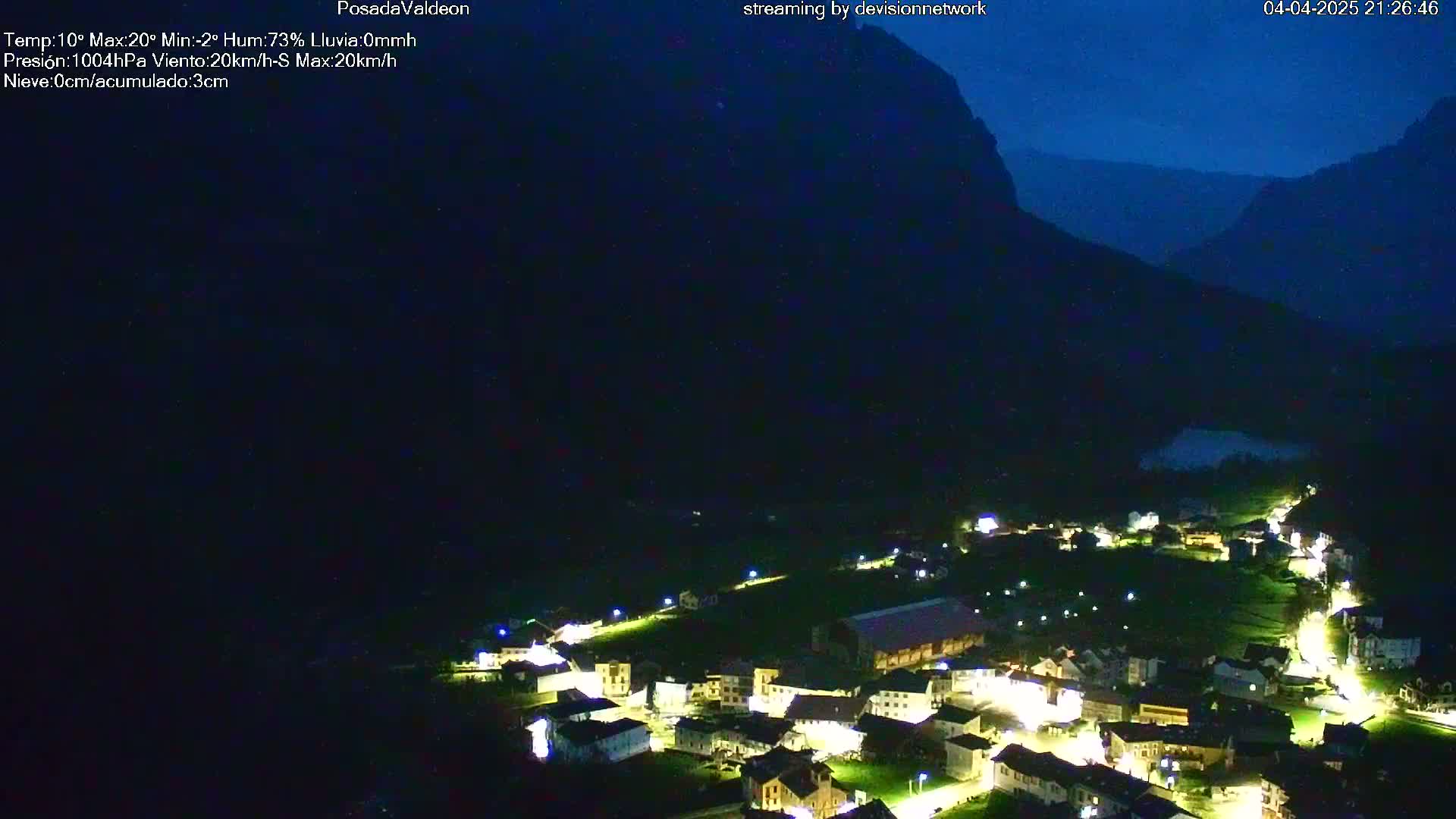 A nighttime view of a small village nestled in a valley between dark mountains under a clear, dark blue sky.
