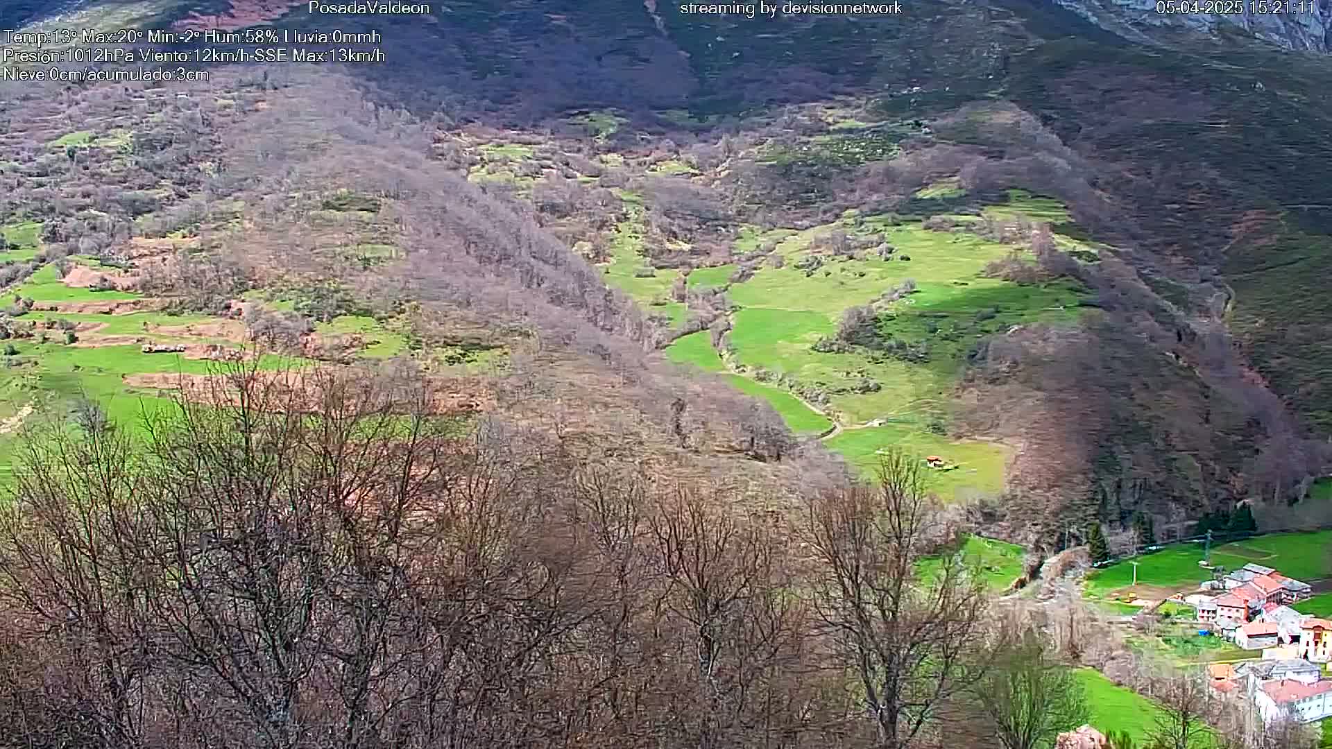 A high-angle view of a valley with green pastures, leafless trees, and a small village nestled amongst the hills on a sunny day.