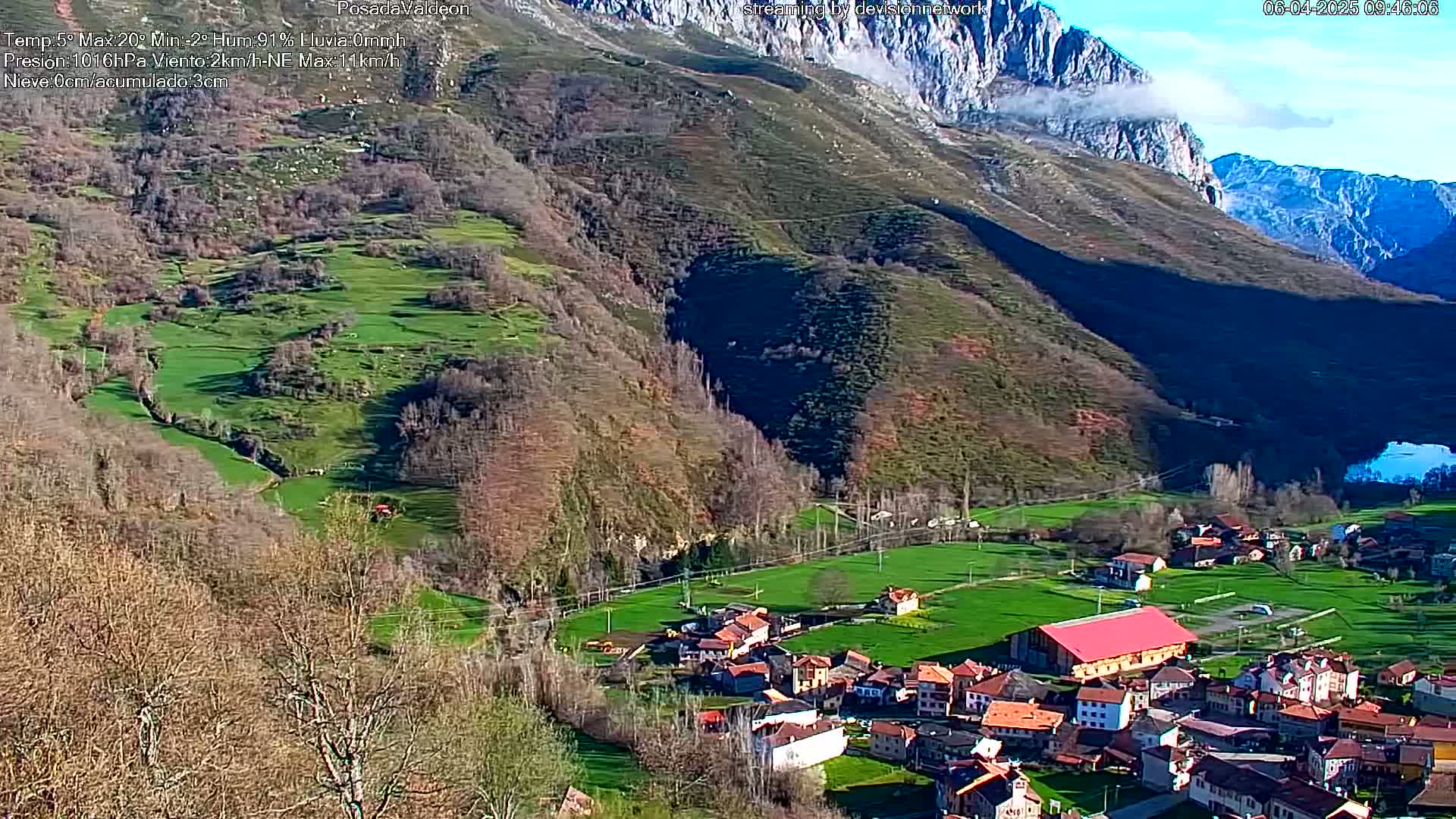 A small village nestled in a valley surrounded by brown and green hills, under a partly sunny sky.