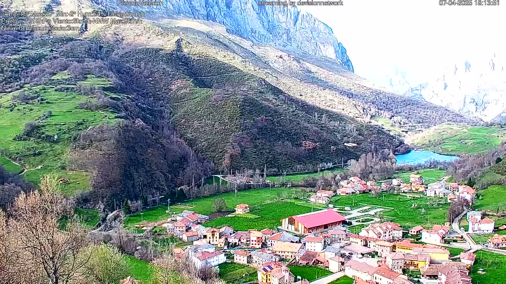 A small village nestled in a valley surrounded by green hills and mountains under a partly cloudy sky.
