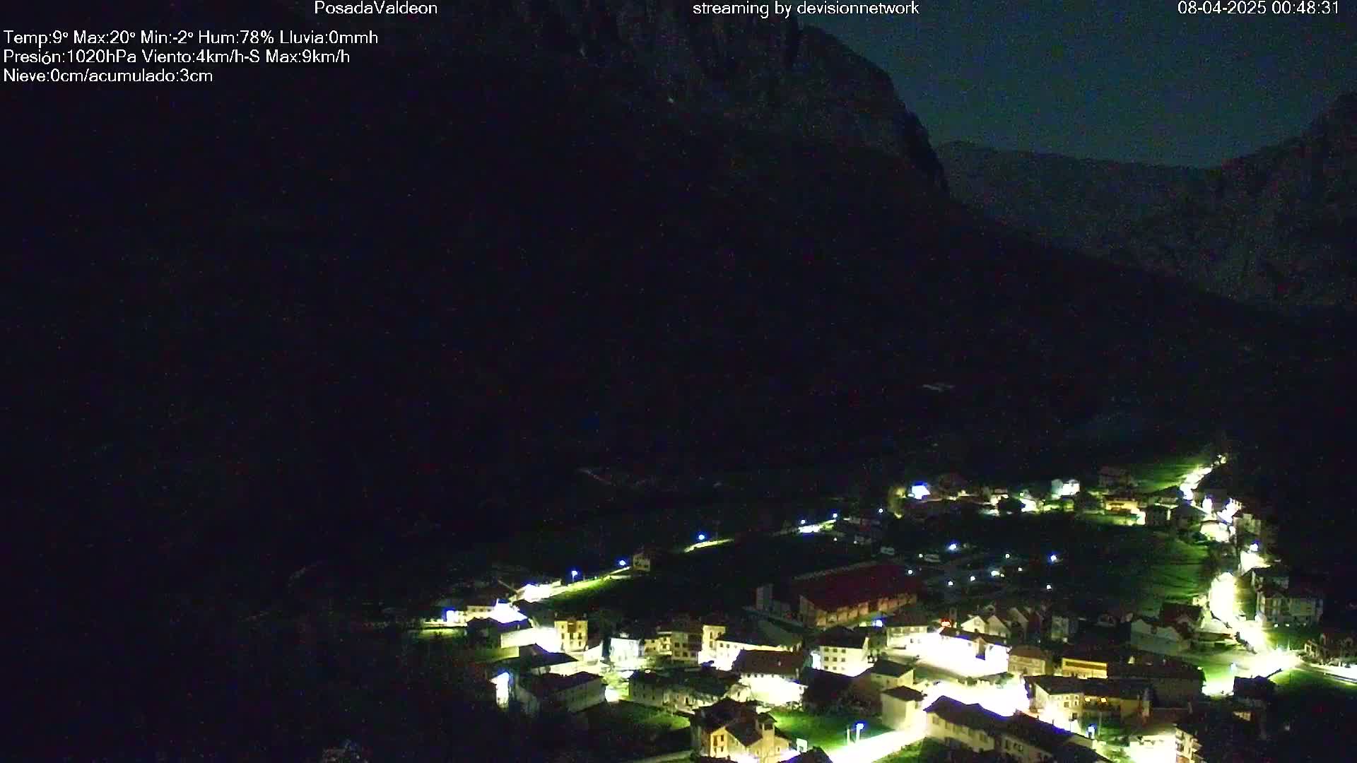 A small village nestled in a valley at night, illuminated by streetlights, under a dark, clear sky.