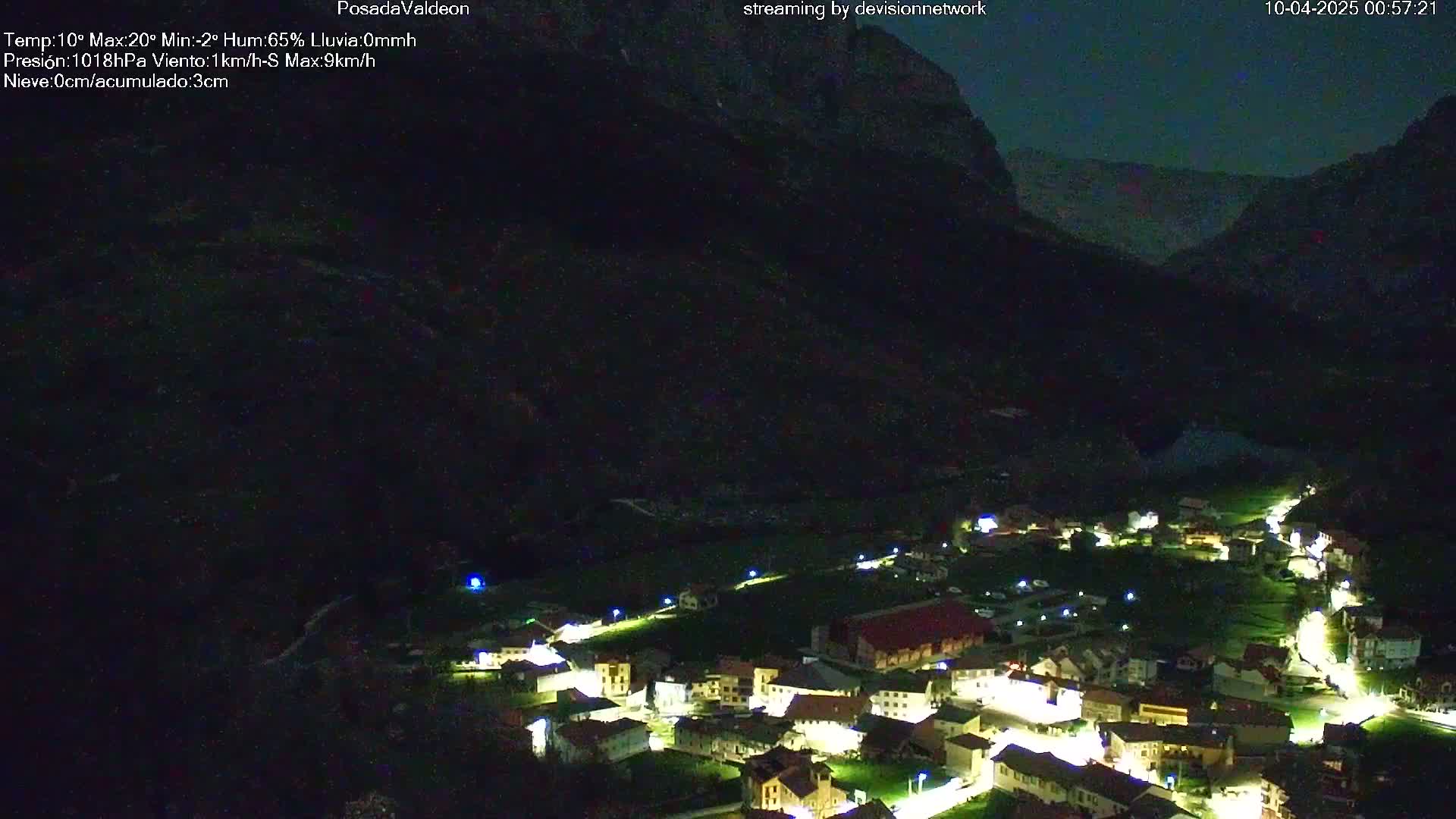 A nighttime aerial view of a small village nestled in a valley, illuminated by streetlights, under a dark, clear sky.