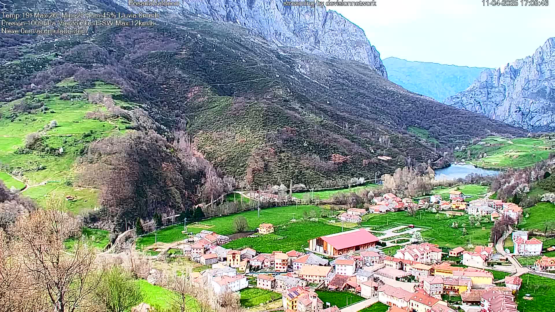 A small village nestled in a verdant valley between mountains, under a mostly clear sky.