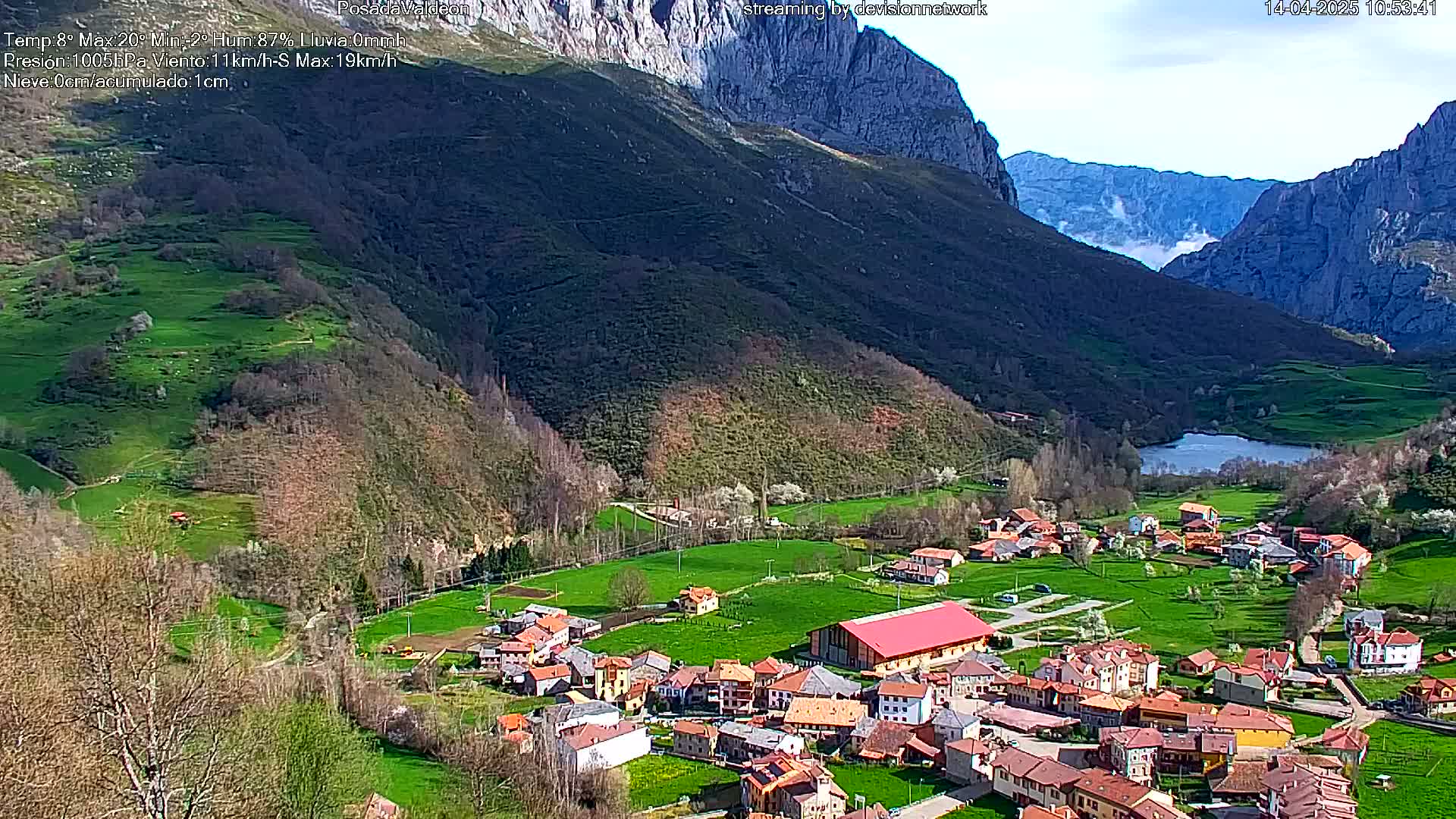 A small village nestled in a verdant valley, surrounded by mountains under a partly cloudy sky.