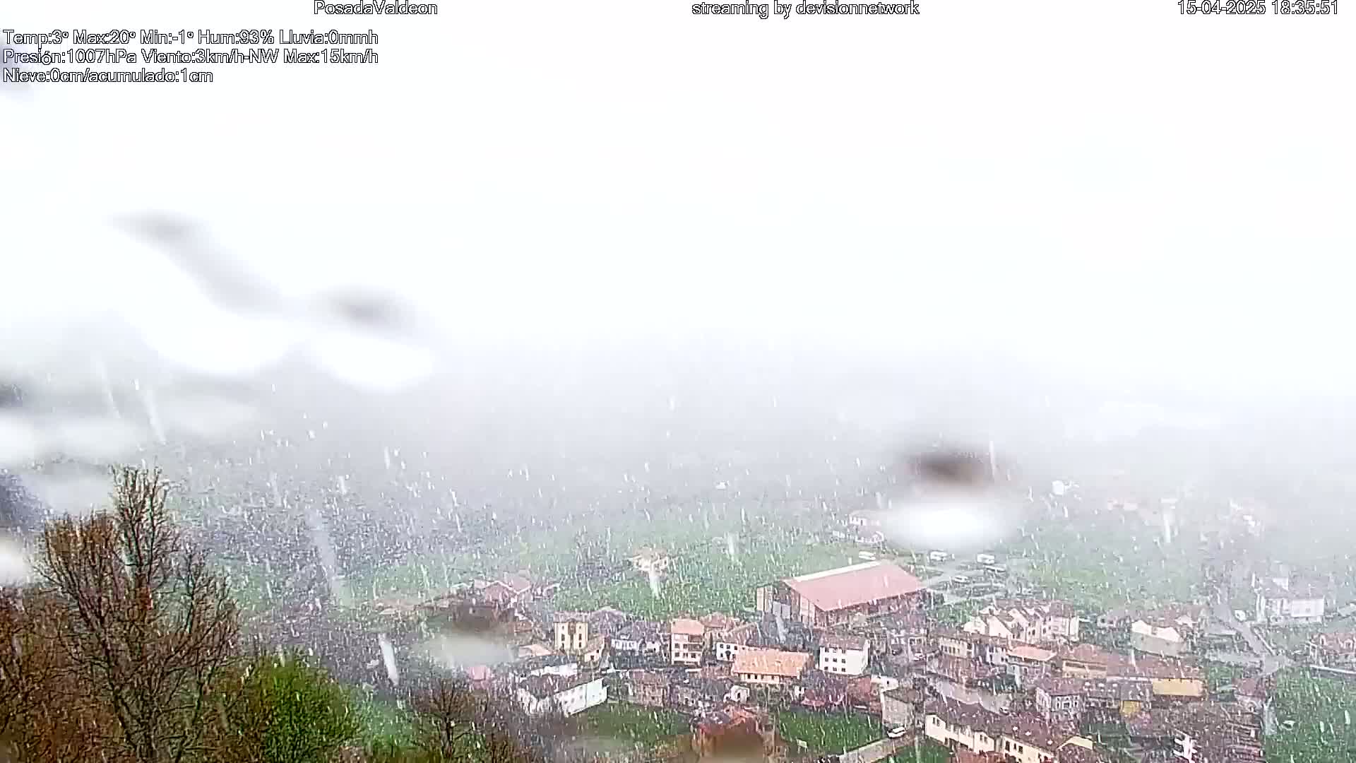 Rain falls on a small village nestled in a valley, partially obscured by the downpour.